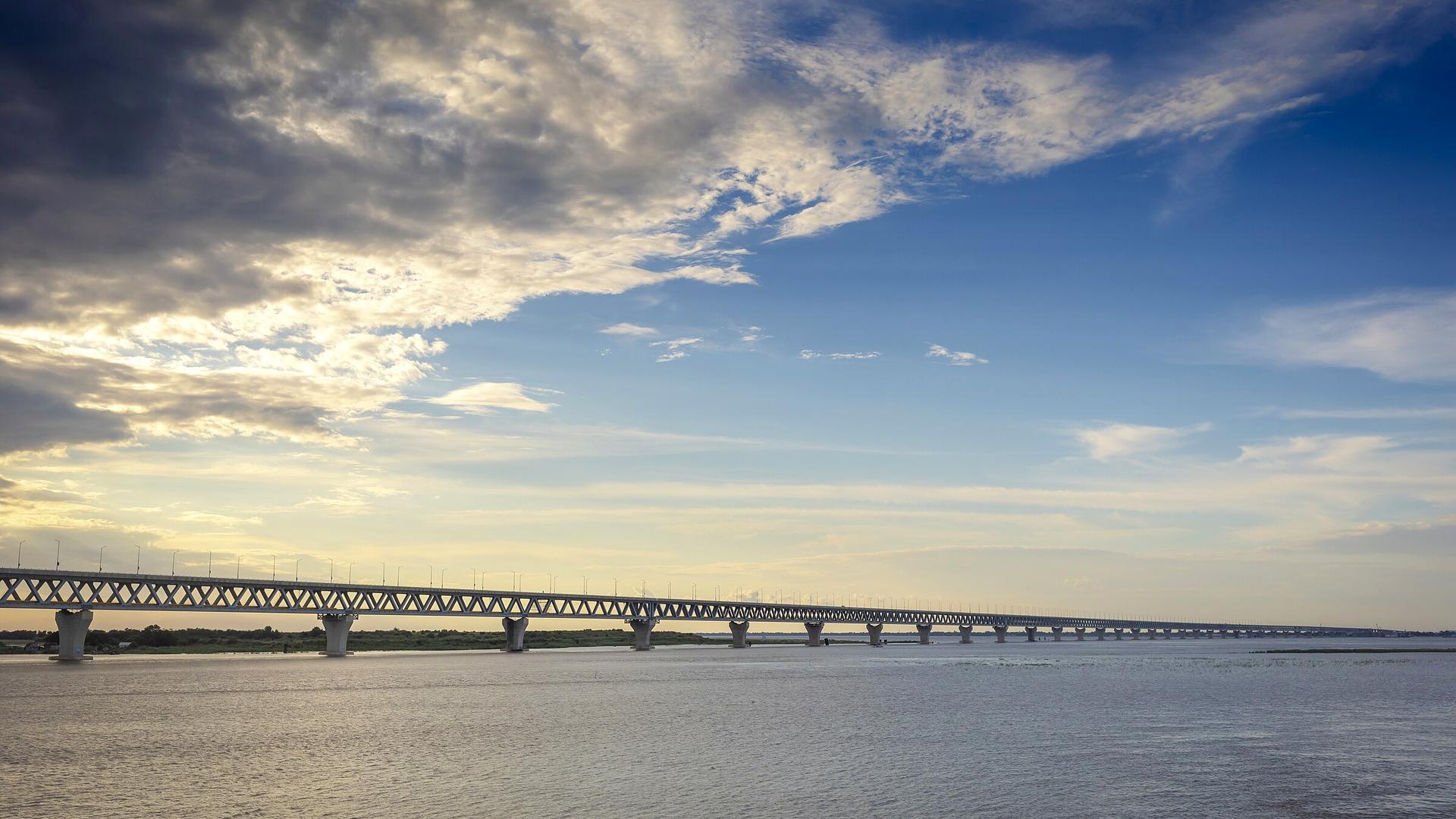 Padma Bridge stretching across the river under a dramatic sky